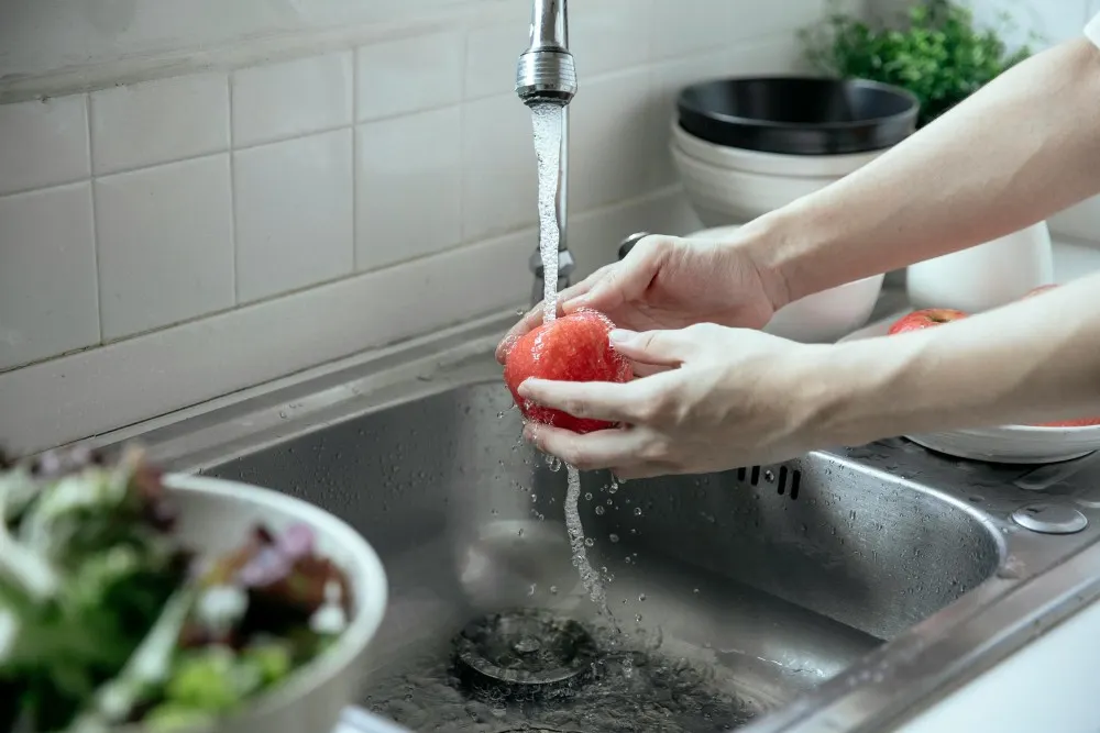 Cô gái rửa rau củ ở bồn rửa trong bếp