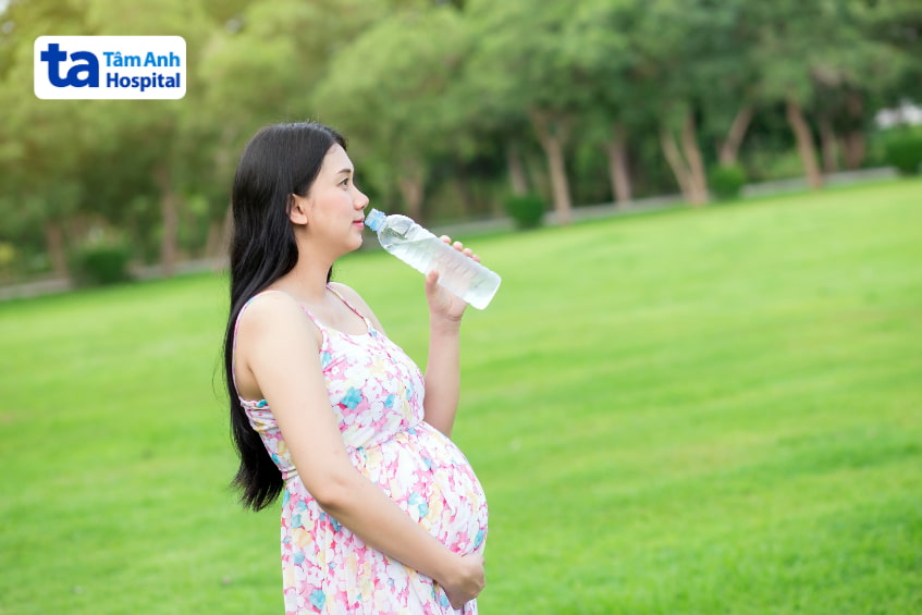 Mẹ bầu mặc váy hoa uống nước trong công viên xanh mát
