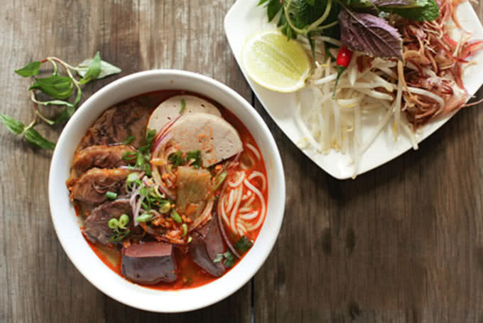 Tô bún bò Huế hoàn chỉnh với rau sống, chanh ớt và nước dùng nóng