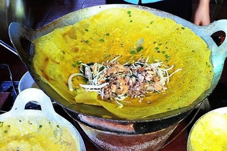 Chiếc bánh xèo vàng ươm, giòn rụm được đổ trên chảo, thể hiện kỹ thuật làm bánh xèo giòn chuyên nghiệp.