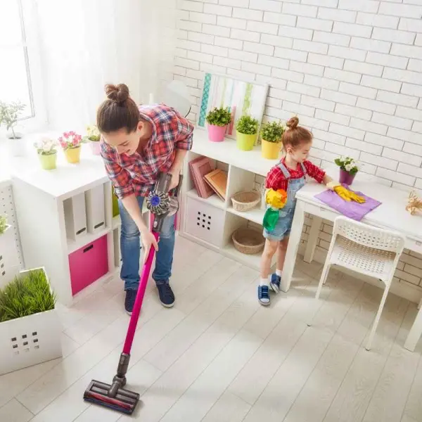 Hình ảnh cho thấy hai người, người lớn đang hút bụi và trẻ em đang lau dọn bàn, trong căn phòng sáng sủa với cây cảnh