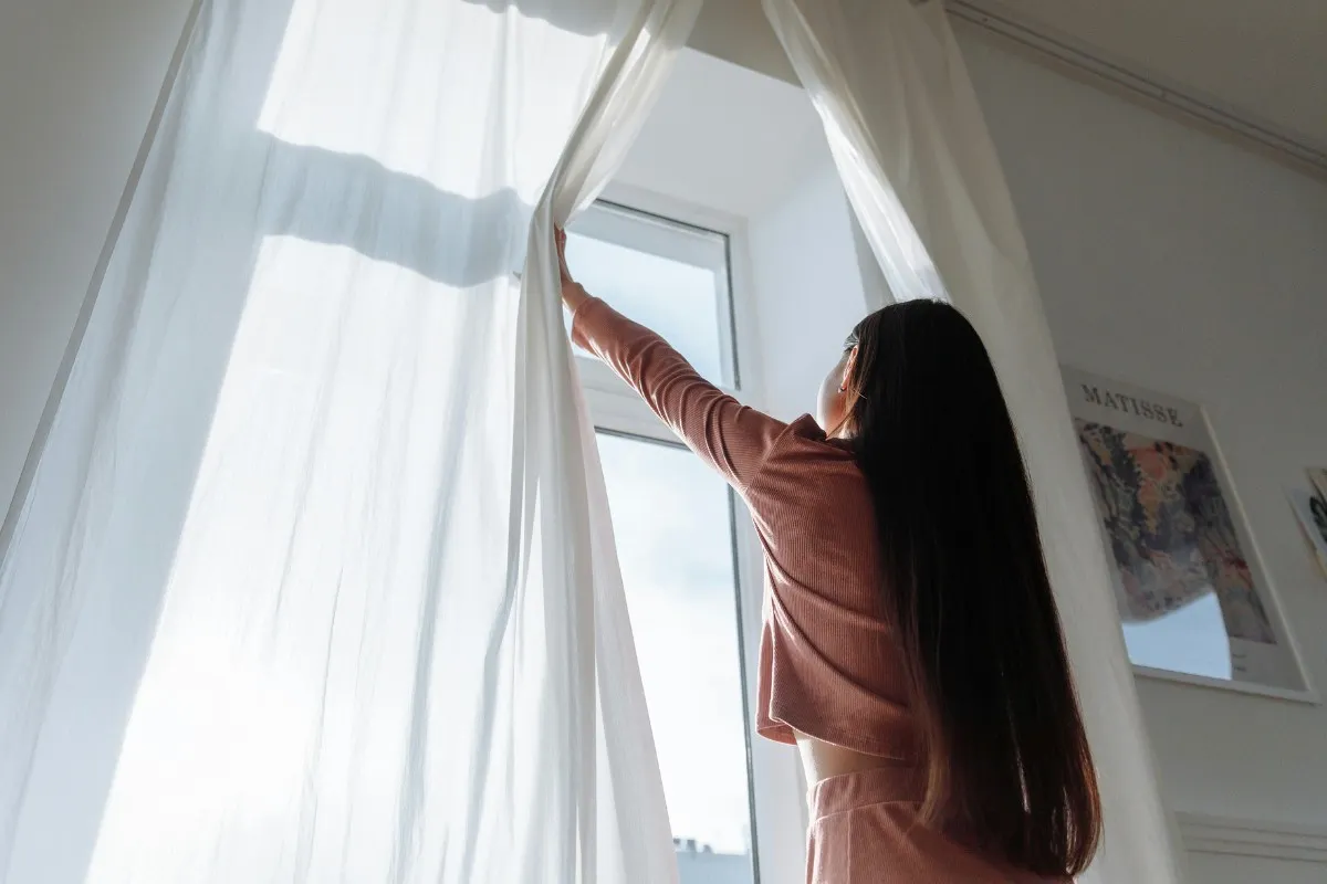Cô gái kéo rèm và mở cửa sổ để nhà cửa thông thoáng