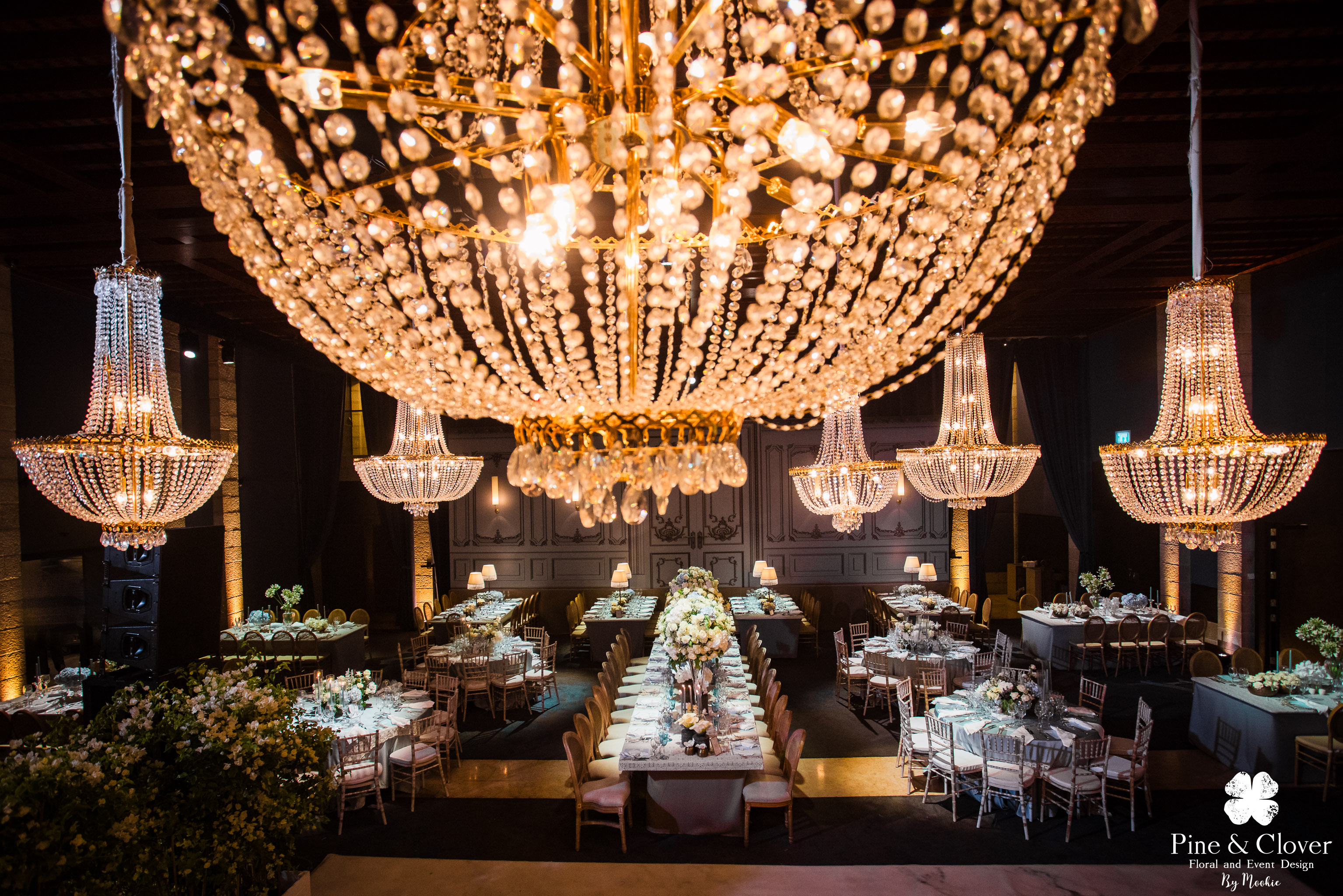 Chiếu sáng hoàng gia với nến tây cao, đèn chùm trần, và ánh sáng vàng ấm từ nhiều hướng