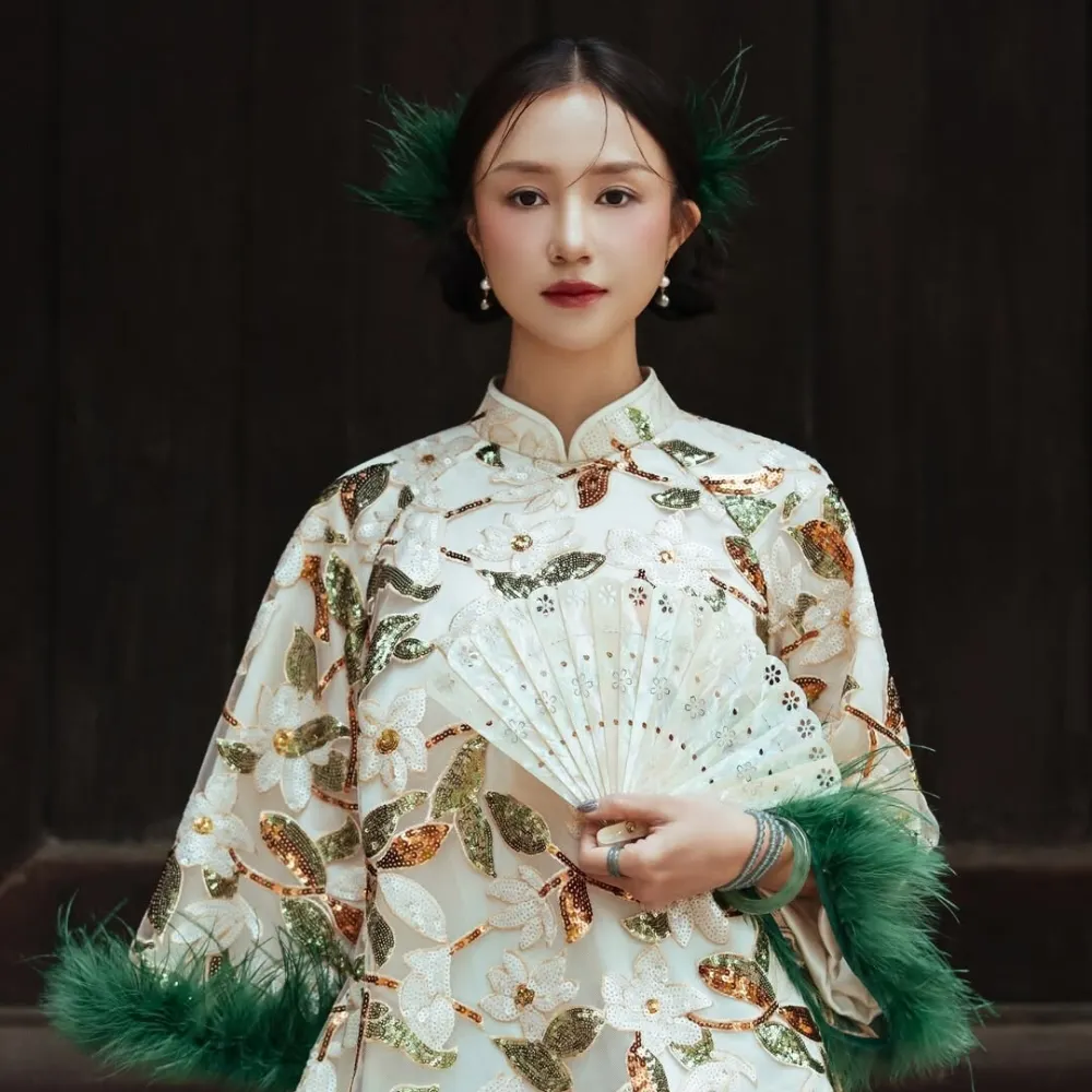 Salim mang áo viền lông xanh cầm quạt tay