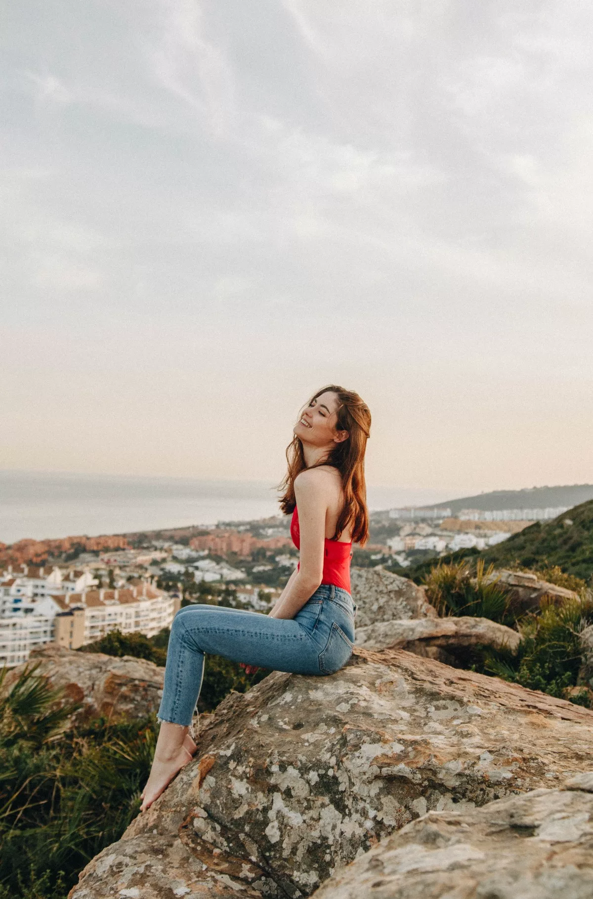 Cô gái mặc quần jeans và áo thun đỏ ngồi trên mỏm đá