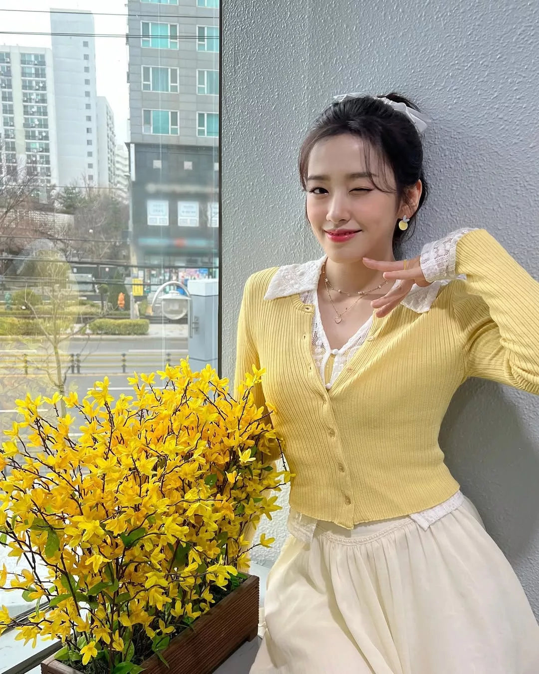Ahn Yujin IVE năng động với áo cardigan vàng pastel ngắm hoa anh đào